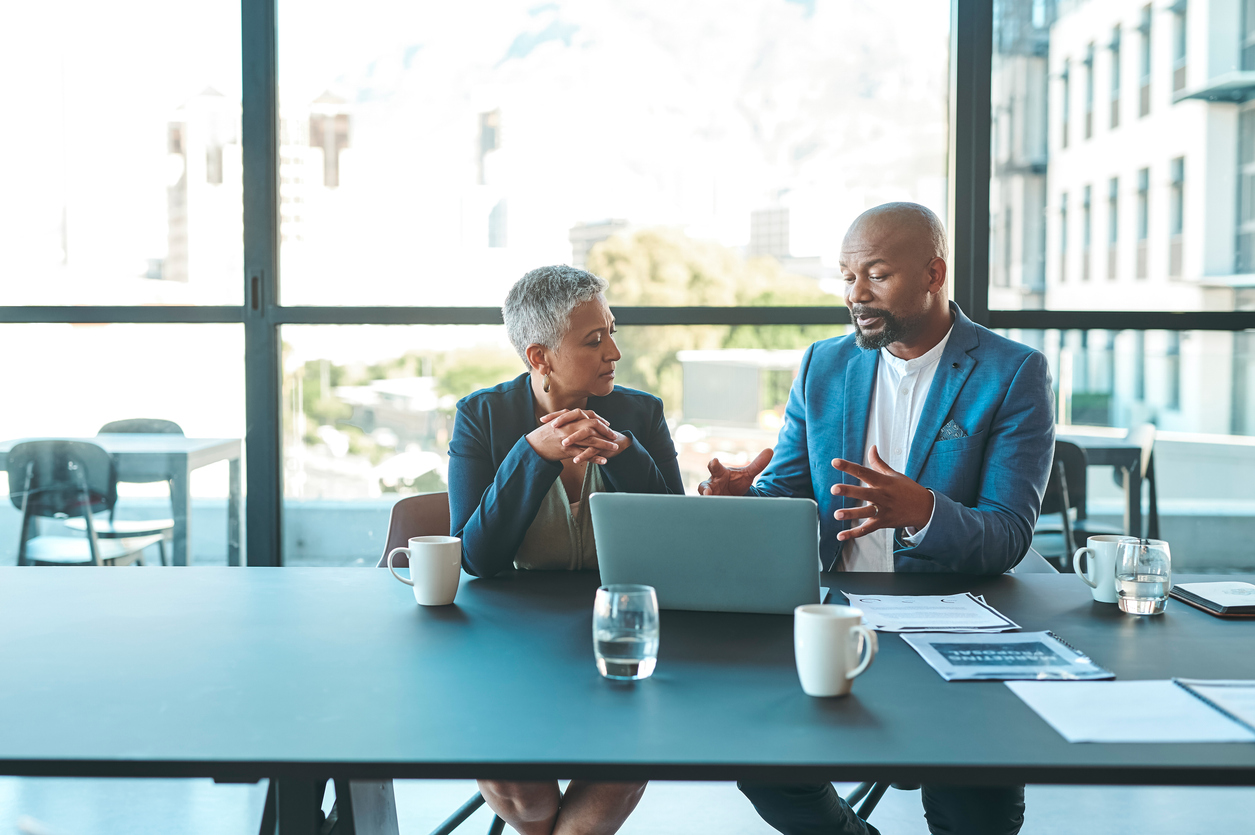 Business person presenting to another professional at a table with a laptop